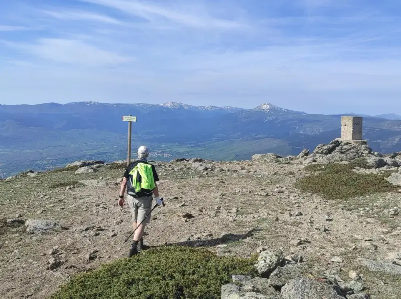 Senderista camina hacia el **puerto de Navafría**, con un mojón y montañas nevadas al fondo.